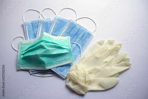 A green surgical face mask is slightly used, on top of blue.  Rubber gloves are all on white background.  Medical objects for Corona virus or Covid 19 protection. 