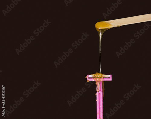 Sugar paste for sugaring or beauty wax flows from a wooden waxing Board to a pink shaving machine. The concept of hair removal . Wax vs razor. Black background. Free space for text.