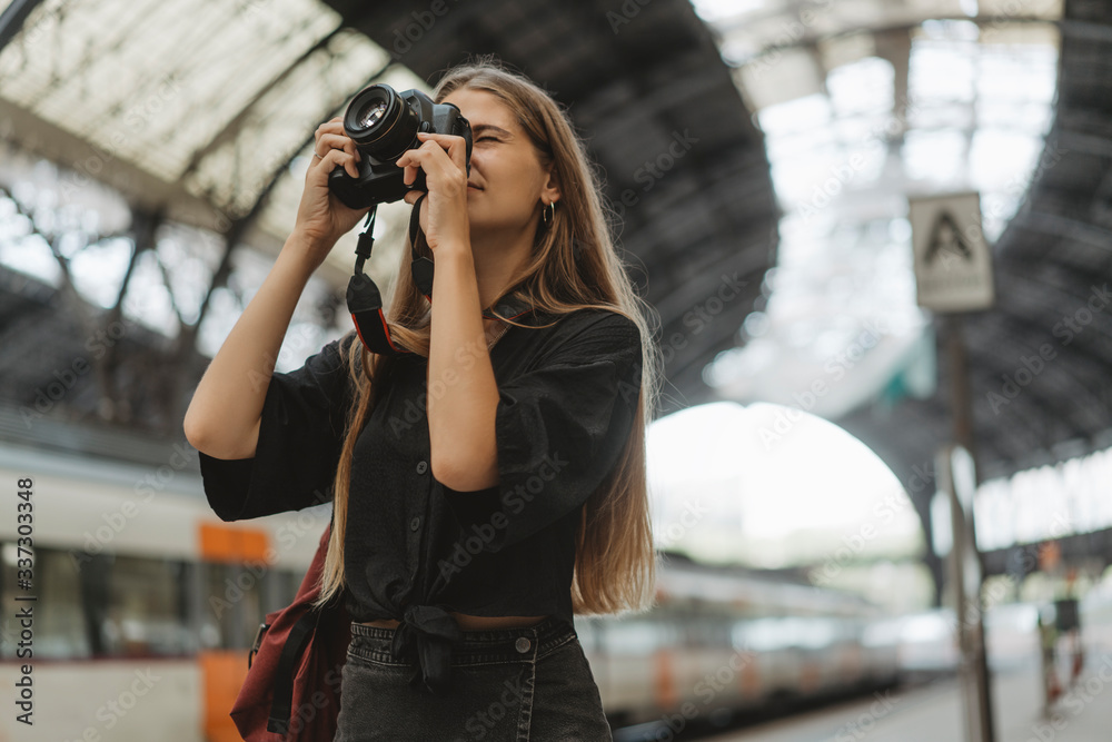 A young girl is a tourist who visits different cities and takes photos of different urban views. At the railway station, a nice young lady with a camera in her hands takes pictures