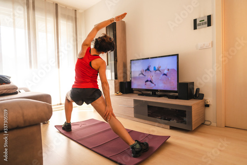 A young Caucasian woman doing stretching in the room following the instructions of the online teacher. Sport in the covid19 quarantine at home