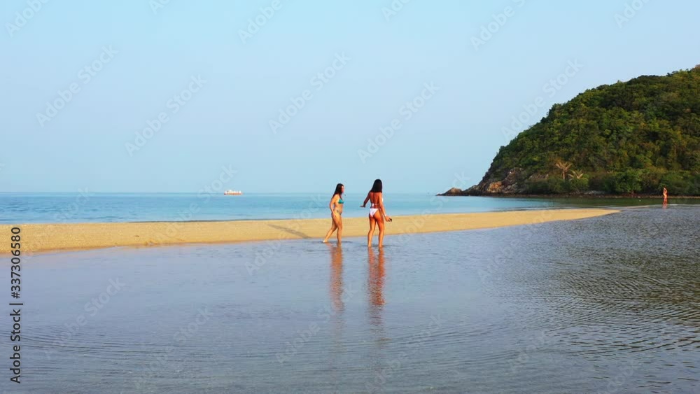 Two beautiful young women in swimsuit walking on shallow water of sea near sandy beach of tropical island in Vietnam Two beautiful young women in swimsuit walking on shallow water of sea near sandy beach of tropical island in Vietnam