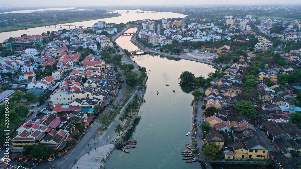 Aerial view of Hoi An old town on Thu Bon river at sunset, Quang Nam province, Vietnam. Unesco world heritage. Many boats moored to shore, bridges, Vietnamese houses on picture.