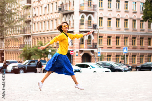 Young beautiful woman in long yellow sweater and blue skirt walking in cozy city street.Full-length portrait of trendy stylish girl in the city.
