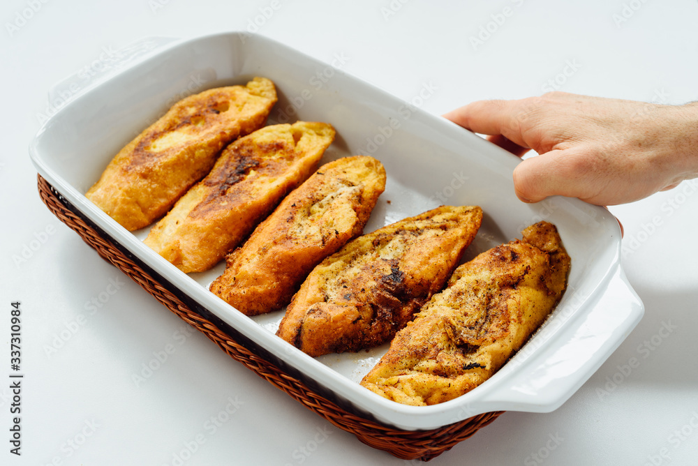 Male hand holding a tray with torrijas, a typical Spanish sweet fried toasts of sliced bread soaked in eggs and milk, on white background Male hand holding a tray with torrijas, a typical Spanish sweet fried toasts of sliced bread soaked in eggs and milk, on white background