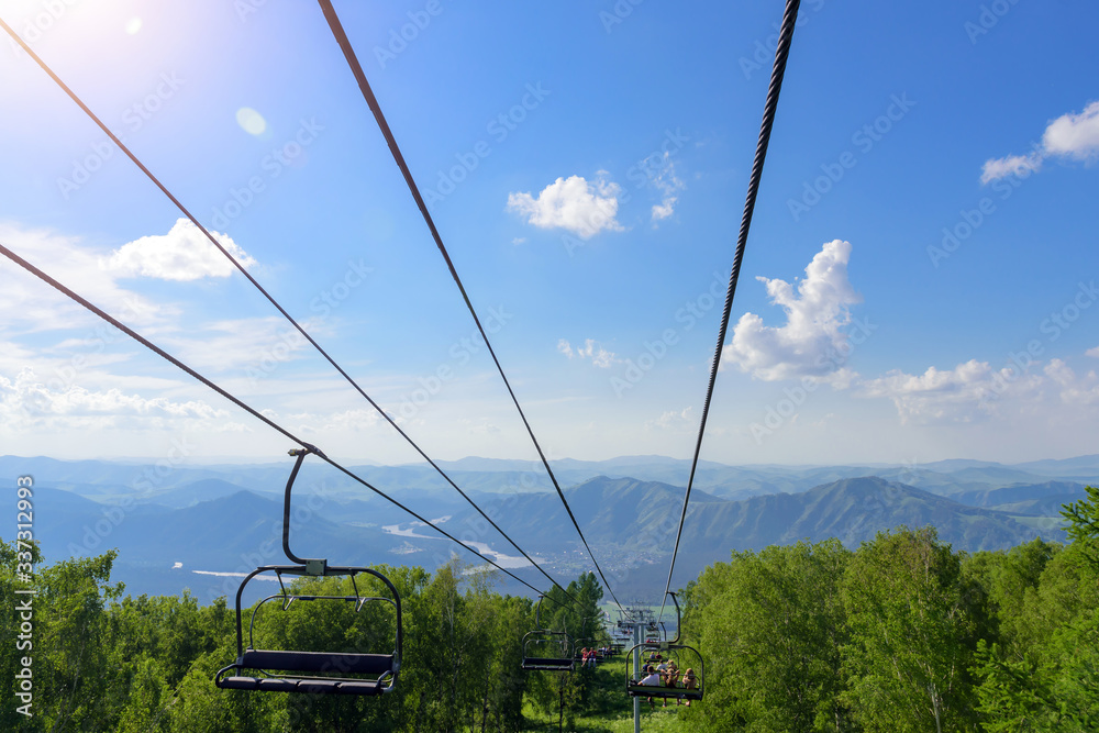 Lift in the mountains on sunny day. Mountain valley with cable car, view from top. Green vegetation in the Altai mountains. Concept of summer vacation.