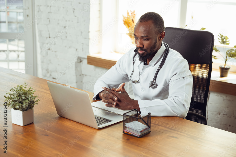 Doctor consulting for patient, calm and cheerful. African-american doctor during his work with patients, explaining recipes for drug. Daily hard work for health and lives saving during epidemic. Doctor consulting for patient, calm and cheerful. African-american doctor during his work with patients, explaining recipes for drug. Daily hard work for health and lives saving during epidemic.