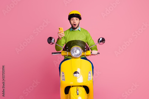 Portrait of his he nice attractive amazed funny cheerful guy riding motorbike using cell reading blog post spending time isolated over pink pastel color background © deagreez
