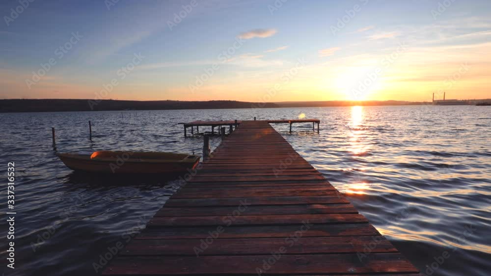 Boat and wooden jetty on lake with a reflection in the water at sunset Boat and wooden jetty on lake with a reflection in the water at sunset