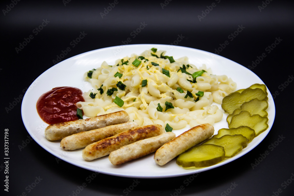Pasta on a plate with cheese on top and green onions. Delicious pasta made from high quality flour with chicken sausage from grill and sliced cucumber from jar. Horns made of flour cooked with cheese