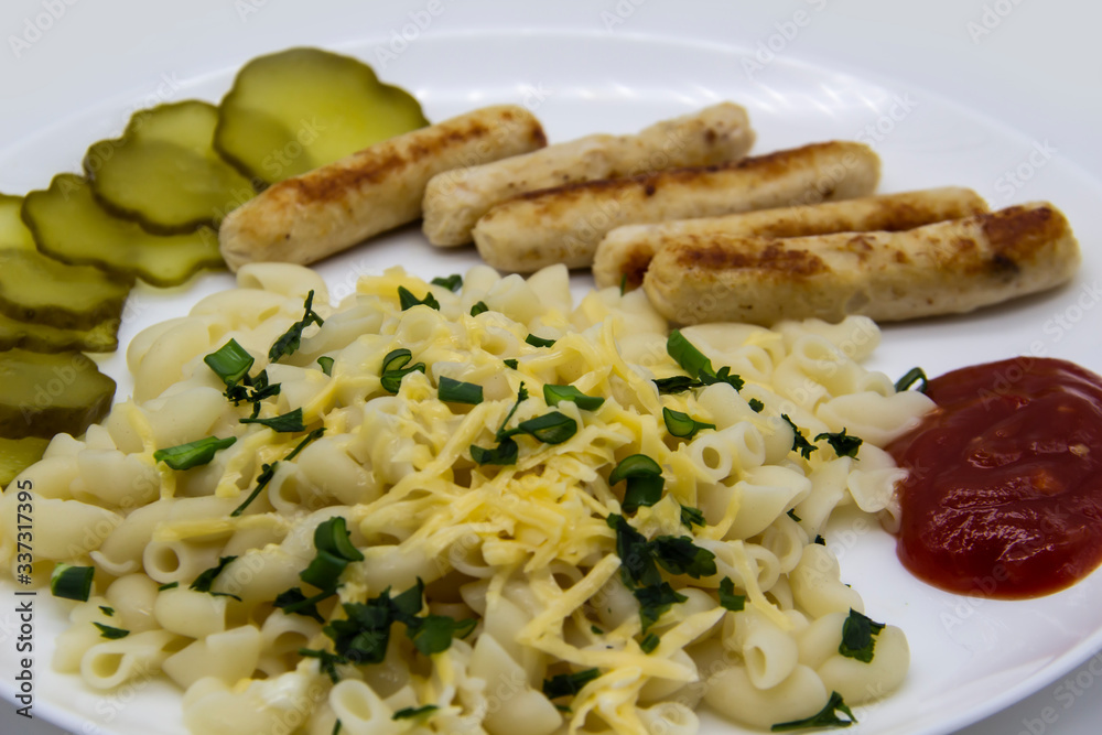 Pasta on a plate with cheese on top and green onions. Delicious pasta made from high quality flour with chicken sausage from grill and sliced cucumber from jar. Horns made of flour cooked with cheese Pasta on a plate with cheese on top and green onions. Delicious pasta made from high quality flour with chicken sausage from grill and sliced cucumber from jar. Horns made of flour cooked with cheese