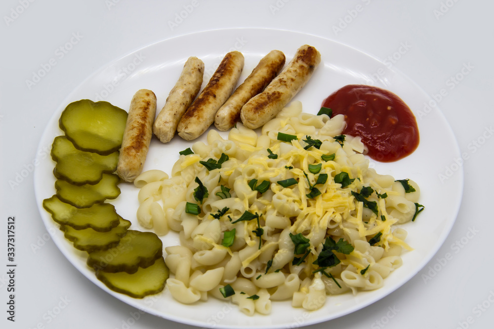 Pasta on a plate with cheese on top and green onions. Delicious pasta made from high quality flour with chicken sausage from grill and sliced cucumber from jar. Horns made of flour cooked with cheese Pasta on a plate with cheese on top and green onions. Delicious pasta made from high quality flour with chicken sausage from grill and sliced cucumber from jar. Horns made of flour cooked with cheese