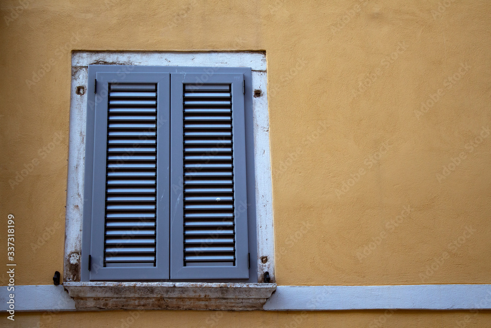 Window with closed shutters on a yellow wall