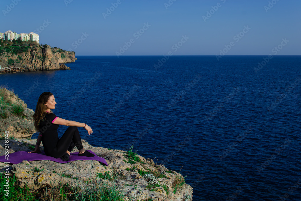 Beautiful young happy girl sitting on rock relaxing and looking to the blue sea