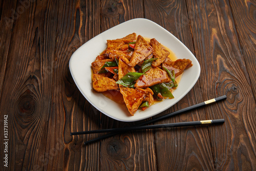 Homemade tofu stir fry with vegetables in hot sweet sauce and pair of chopsticks on dark wooden background and copy space. Asian food concept top view