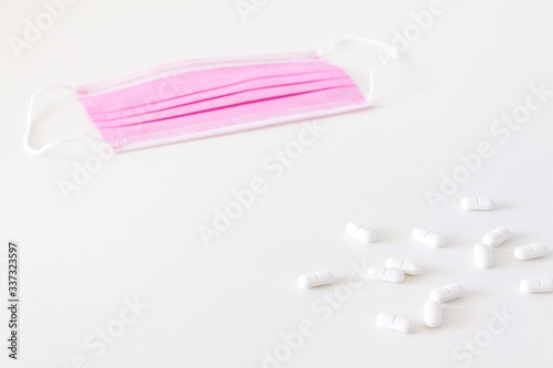 Disposable surgical mask and white scattered pills on a white background.