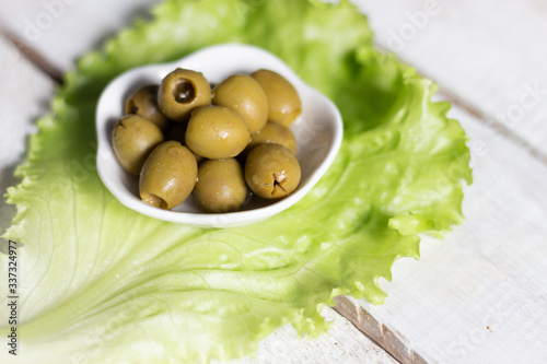 Quadro em tela Green olives seedless in white bowl on salad leaf on   wooden background close u