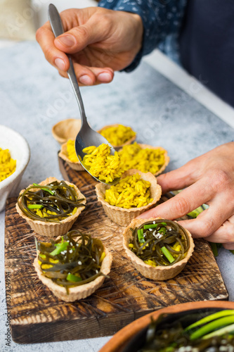 Woman hands make vegan tarts with long rice filling and stuffed with laminaria kelp seaweed salad. Healthy snack. 