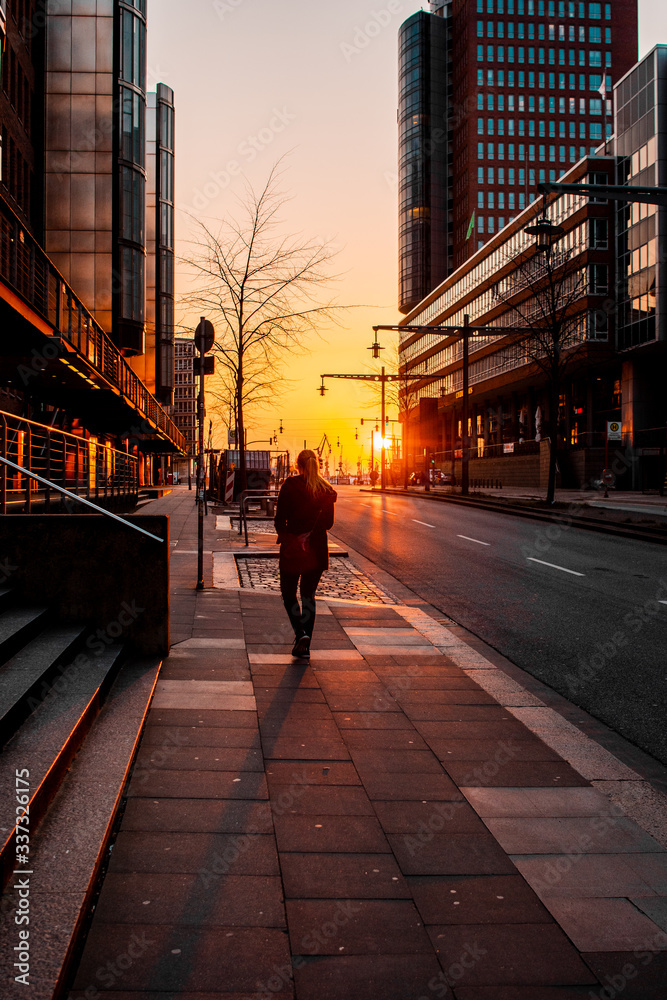 Silhouette backview of a girl walking in the empty streets at low evening sunset light. Historic and famous harbour district Speicherstadt and modern Hafencity  in Hamburg, Europe