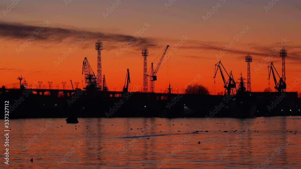 Sunset over the sea and industrial cranes, birds in the water and lights Sunset over the sea and industrial cranes, birds in the water and lights