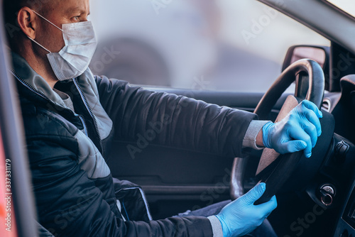 A man driving a car in a protective medical mask and gloves. Safe drive in a taxi during a pandemic coronavirus. Protect the driver and passengers from bacteria and virus infection in quarantine