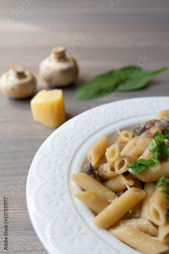 Vegan creamy mushroom garlic pasta with red onions garnished with basil in a white plate with its ingredients in the background, everything on the gray wooden surface