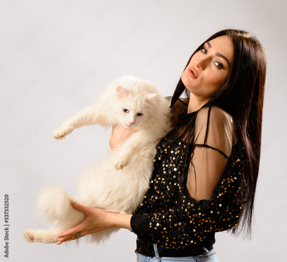 Portrait on a white background of a glamorous young brunette woman with fashionable make-up in a shiny sweater with a white cat in her hands Portrait on a white background of a glamorous young brunette woman with fashionable make-up in a shiny sweater with a white cat in her hands