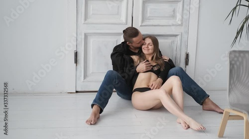 erotic couple flirting at home sitting on floor.men's hands touch women's legs and body.woman in black underwear and shirt kisses brutal man with beard and mustache.Sunny day,4k