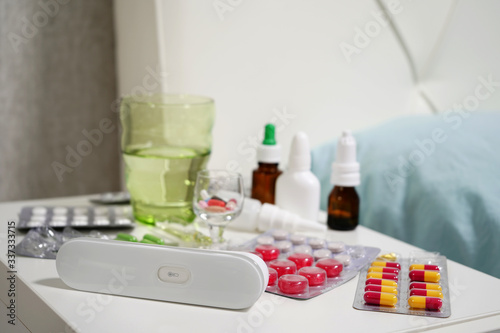 Contactless thermometer, and various pills and medications on the bedside table in close-up.