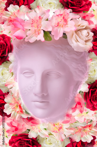 Fototapeta Naklejka Na Ścianę i Meble -  Beautiful young female face and colorful flowers. Plaster antique bust of Venus in a floral wreath. Beauty spring and summer model girl with fresh bouquet.