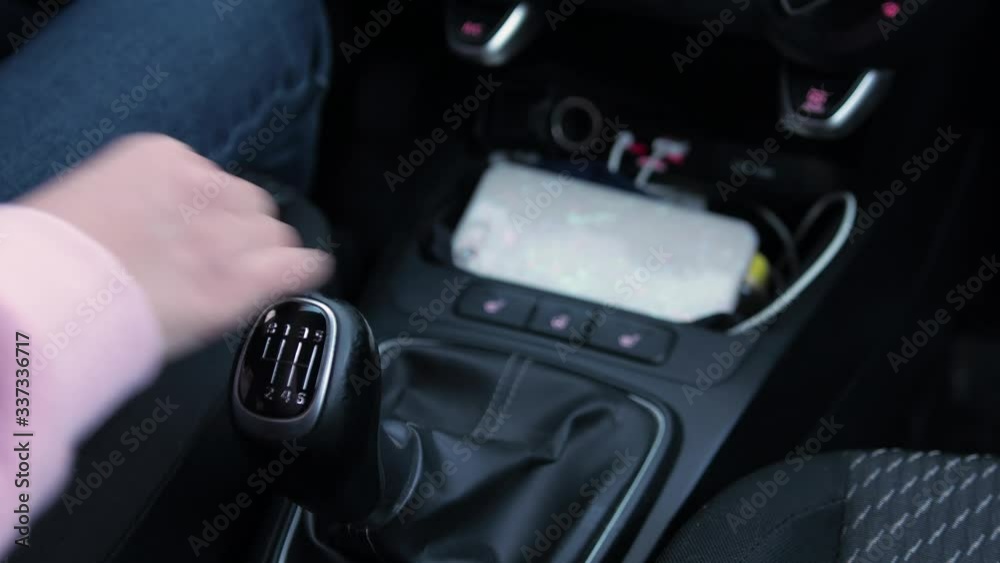 Girl's hand in pink pite shifts a manual gearbox in a car.