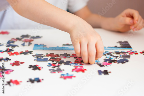 The child collects a puzzle. Elements of the puzzle are laid out on a white table. Children's hands during the game. Home leisure.