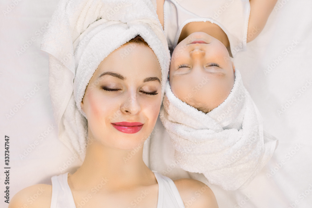 Top view of beautiful young mother and her two year old daughter lying on the bed at home, relaxing after nice spa bath procedures with eyes closed. Family spa and beauty care Top view of beautiful young mother and her two year old daughter lying on the bed at home, relaxing after nice spa bath procedures with eyes closed. Family spa and beauty care