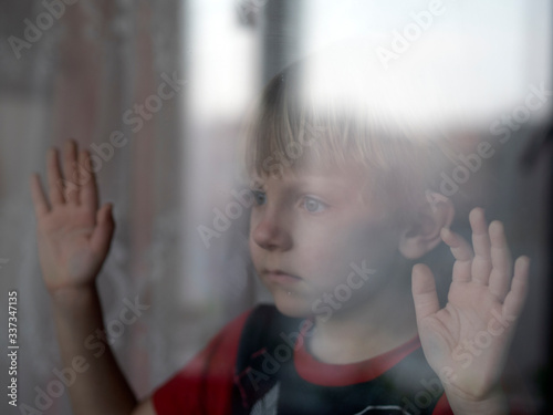 The boy looks at the street through a closed window.