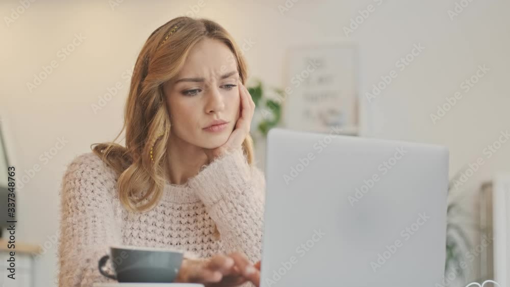 A serious displeased young woman is typing on her laptop computer in a cozy cafe indoors A serious displeased young woman is typing on her laptop computer in a cozy cafe indoors