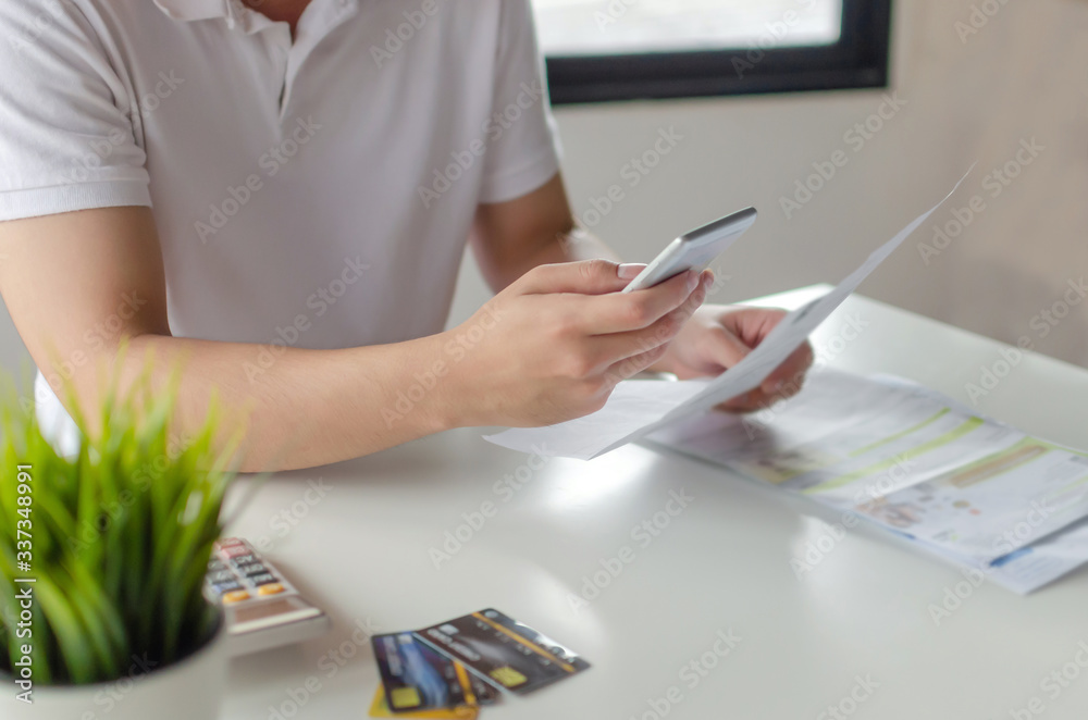 Fototapeta premium hand of young man using mobile smart phone for scan and payment online with family budget cost bills on desk in home office, plan money cost saving, investment, business finance, expenses concept