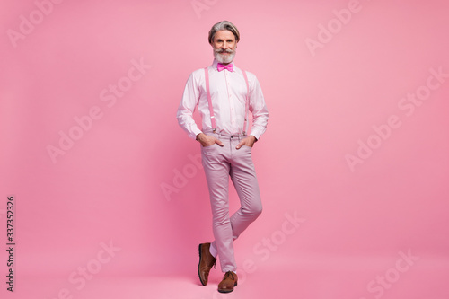 Full length body size view of his he nice attractive well-dressed imposing elegant cheerful cheery content grey-haired man holding hands in pockets isolated over pink pastel color background