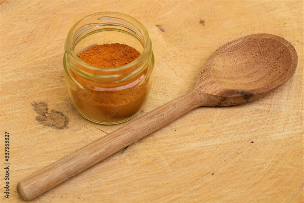 Turmeric powder (Curcuma longa) on a wooden spoon and glass pot on wooden board. Turmeric powder (Curcuma longa) on a wooden spoon and glass pot on wooden board.