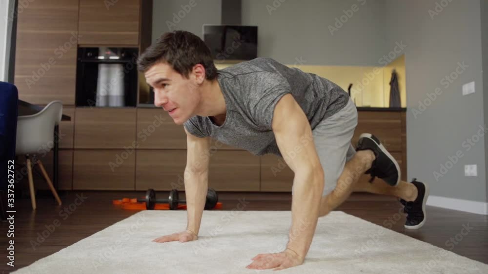 Slow motion shot of determined young man shouting while doing running plank exercise during workout at home