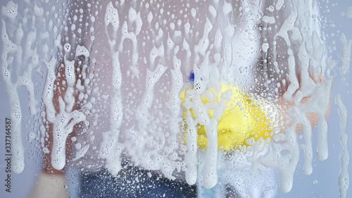 Woman wearing rubber glove spraying soap on window glass cleaning it with squeegee