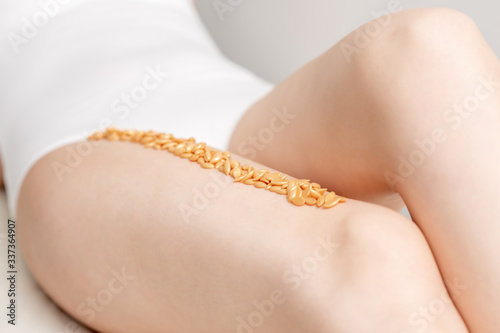 Wax beans orange color on leg of woman in row. Concept of depilation or epilation.