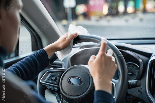 Hands of woman uses disinfectant spray on steering wheel in her car