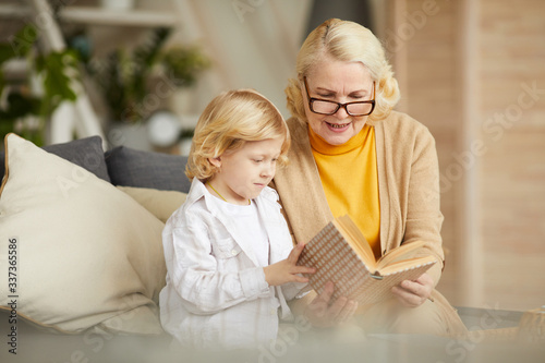 Grandmother in eyeglasses reading a book to her son during their leisure time at home © AnnaStills