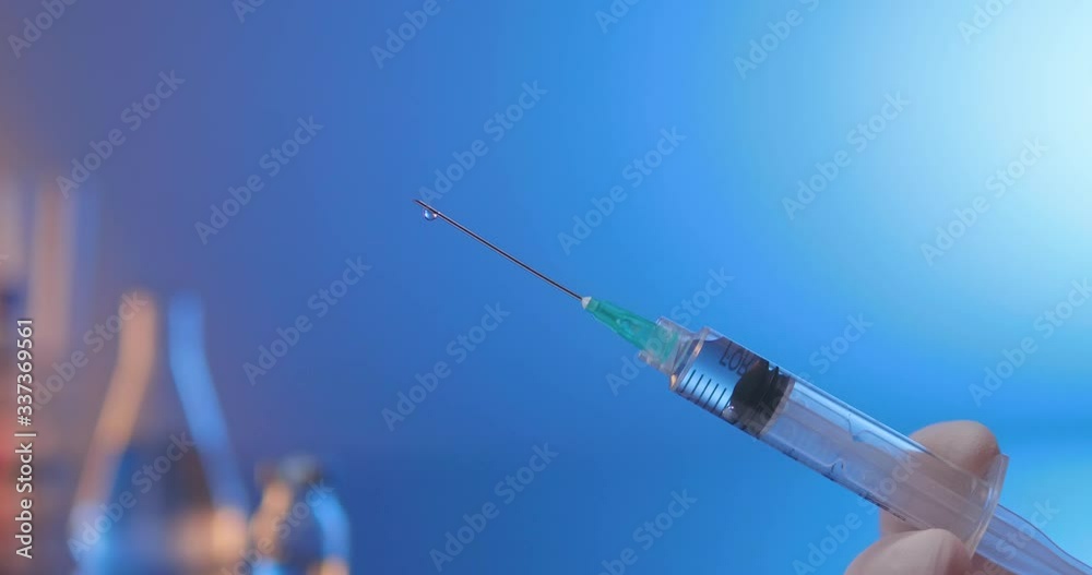 Removing air from syringe filled with vaccine. Close-up side shot on a blue laboratory background.