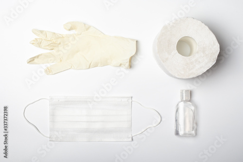 Sterilized medical face mask, antiseptic hand sanitizer, rubber hand gloves and toilet paper on white background. Healthcare basic equipment for battle of Covid-19 epidemic.