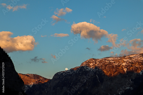 A beautiful picture of a moon slowly hiding behind the mountains with colorful clouds in Hallstatt