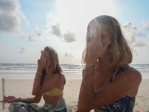 Two yoga girls making nadi shodhana pranayama therapeutic exercise in sunlight photo