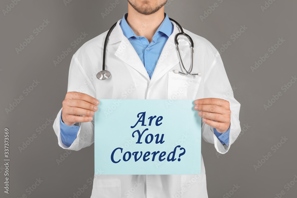 Doctor holding paper with text ARE YOU COVERED? on grey background, closeup. Insurance concept Doctor holding paper with text ARE YOU COVERED? on grey background, closeup. Insurance concept