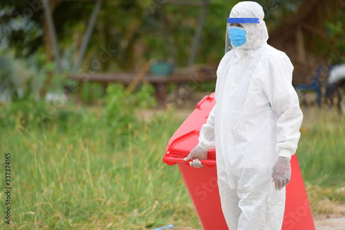 Man in protective suit with red infection bin and infection waste bag Dangerous waste infected Recoleccion de residuos peligrosos e infección con el virus Covid 19. photo