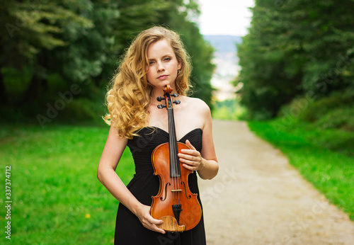 Gorgeous woman with a violin in her hands. Portrait of a beautiful woman outdoors.