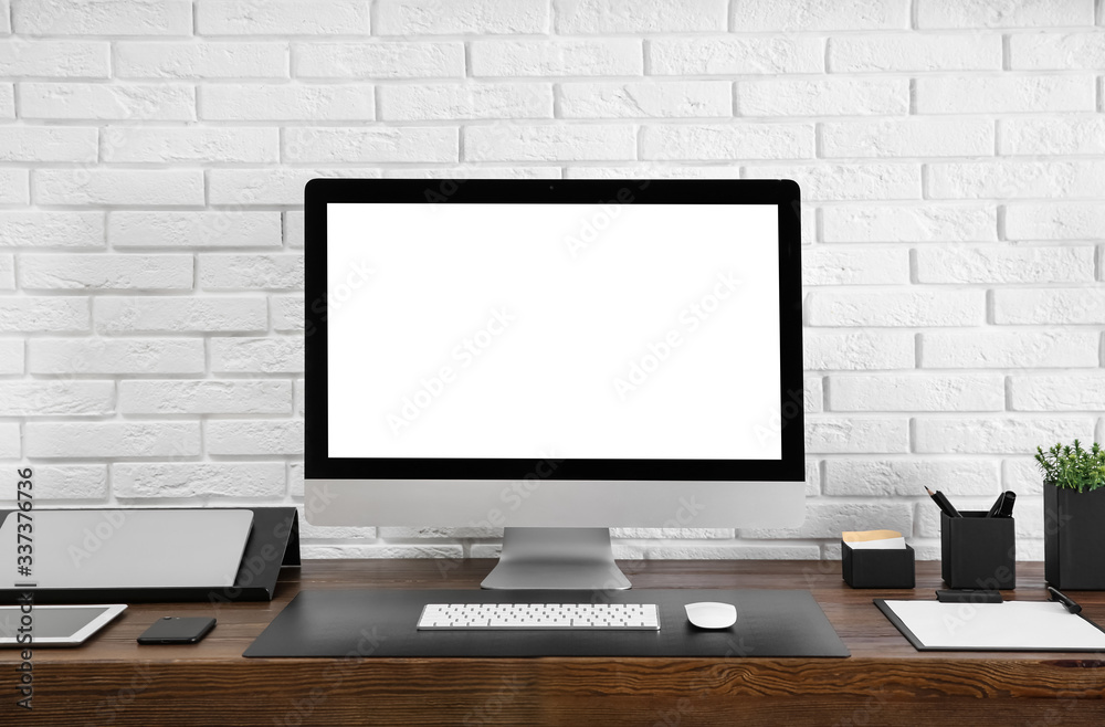 Modern computer with blank screen on table near brick wall. Space for design Modern computer with blank screen on table near brick wall. Space for design